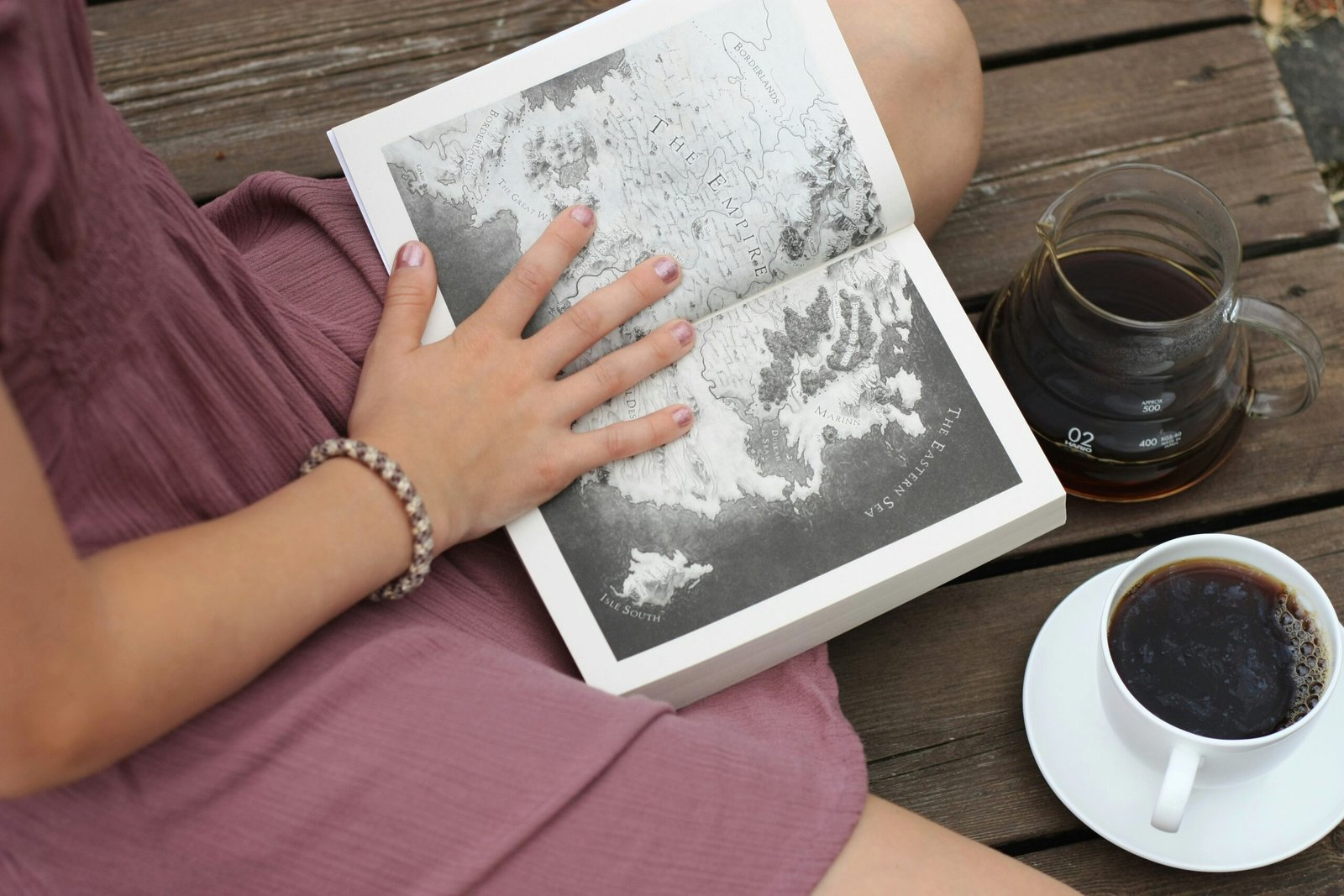 open book to map page on lap of woman in purple dress with a cup of coffee